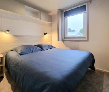 Chambre avec lit double et fenêtre dans le mobil home tout confort du parc résidentiel de loisirs