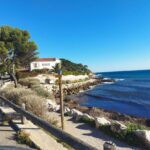 Bord de mer rocheux avec eau bleue et bâtiment en arrière plan du mobil home tout équipé