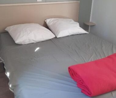 Chambre double avec lit, draps gris et plaid rouge dans le MobilHome de Charlotte