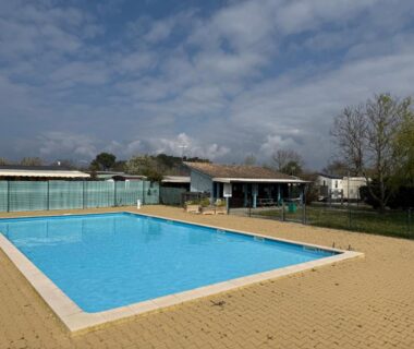 Piscine extérieure avec terrasse et mobil-homes en arrière-plan au MobilHome de la Coccinelle