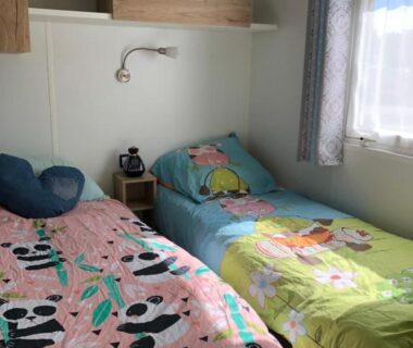 Chambre avec deux lits rideau et lampe dans le mobile home Les Dunes de Contis