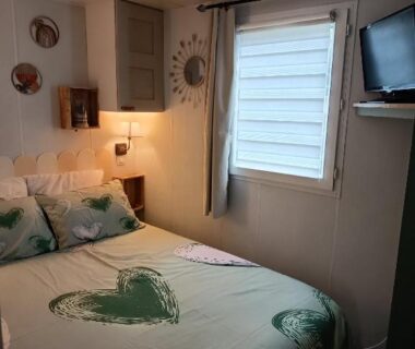 Chambre avec lit à couette motifs cœur et télévision dans le mobile home