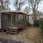 Allée du camping avec terrasse en bois et hublot du mobile home