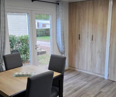Séjour avec table, chaises et baie vitrée dans le Mobile home 4 à 6 personnes du Domaine de Kerlann