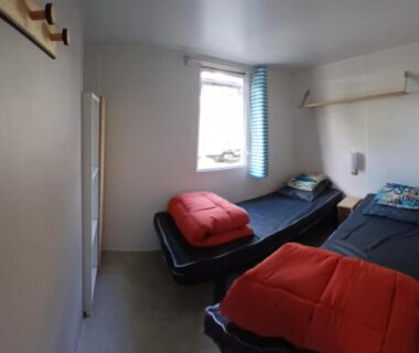 Chambre avec deux lits et couettes rouges dans le mobile home