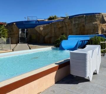 Piscine extérieure avec toboggan et chaises empilées au Mobile home Drôme homair