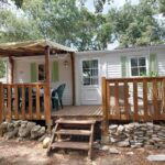 Terrasse en bois avec mobil-home et chaises sous les arbres au Mobile home camping Ardèche