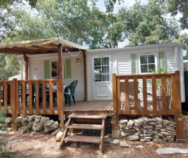 Terrasse en bois avec mobil-home et chaises sous les arbres au Mobile home camping Ardèche
