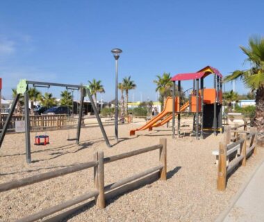 Aire de jeux avec toboggan et balançoires au camping face aux palmiers du mobile-home les pieds dans l'eau