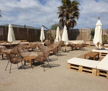 Terrasse extérieure avec chaises parasols banquettes et palmiers du mobile-home les pieds dans l'eau
