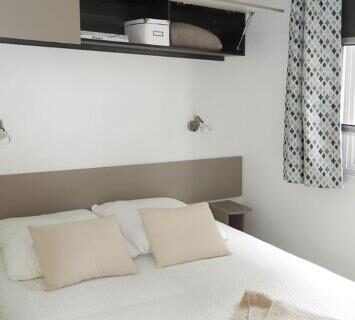 Chambre avec lit double étagère et rideau dans le mobilhome Les Dunes de Contis