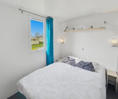 Chambre avec lit double et fenêtre donnant sur le camping dans le Mobilhome