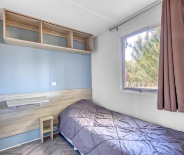 Chambre simple avec lit et bureau près de la fenêtre dans le mobilhome Camping Siblu les Viviers