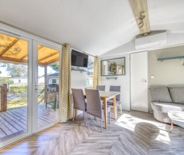 Intérieur lumineux avec terrasse en bois et coin salon dans le Mobilhome Camping Siblu les Viviers