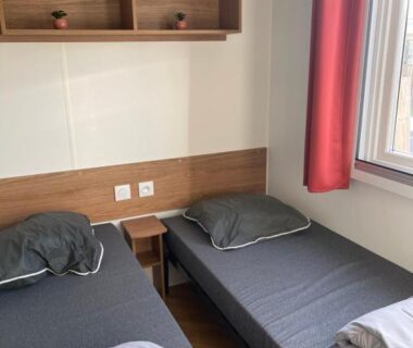 Chambre avec deux lits simples et étagères près de la fenêtre dans le mobilhome Sables du midi