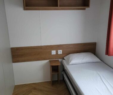 Intérieur chambre avec lit simple étagère et chevet dans le Mobilhome au bord de l'eau