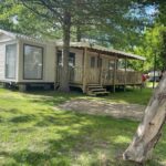 Terrasse en bois et pelouse sous les arbres du Mobilhome bord du lac