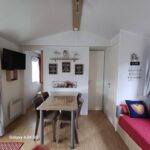Coin repas intérieur avec table chaises et canapé dans le mobilhome camping Ernest Renan Louannec