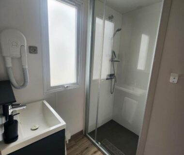 Salle de bain avec douche vitrée lavabo et sèche-cheveux dans le mobilhome Mobilhome dans les pins au Camping Les Oyats