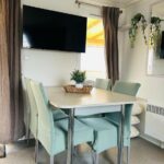 Coin repas avec table chaises télévision et rideaux dans le mobilhome la Carabasse