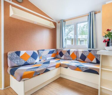 Intérieur salon avec banquette, fenêtre et coin cuisine du Mobilhome - piscines - terrasse