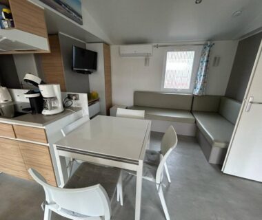 Séjour avec table, chaises, kitchenette et banquette dans le mobilhome sur camping 4 étoiles