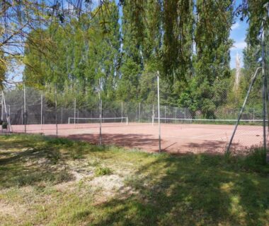 Terrain de tennis en terre battue entouré d'arbres au Mobilhomes Cozy 2 ou 3 chambres en bordure d'étang