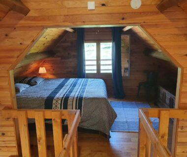 Chambre mansardée en bois avec lit double et fenêtre au Moulin Du Pommier