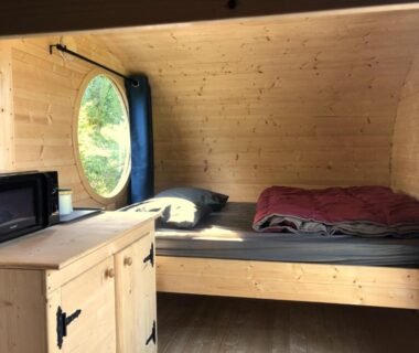 Intérieur en bois avec lit et hublot dans la nuit insolite Côte de granit rose Camping Armor Loisirs