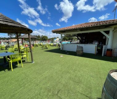 Terrasse extérieure avec bar et pelouse près de la piscine au camping Natuara L'horizon du lac Wifi inclu