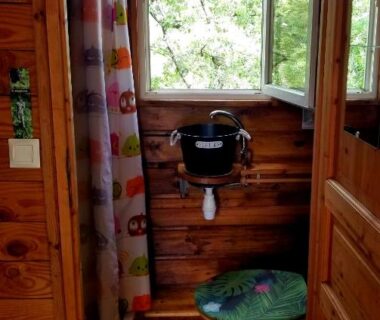 Salle de bains en bois avec toilettes et fenêtre donnant sur la verdure dans le Natura Lodge