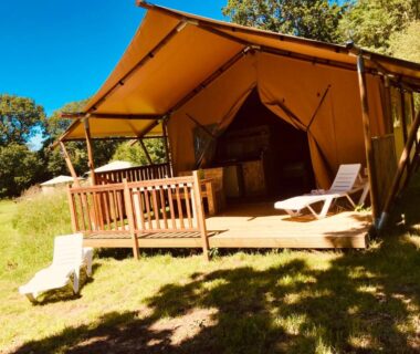 Terrasse en bois avec transats devant tente lodge dans un espace herbeux à O2 Camping
