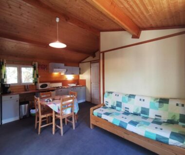 Intérieur de chalet avec coin cuisine et canapé-lit au camping Oasis des Garrigues