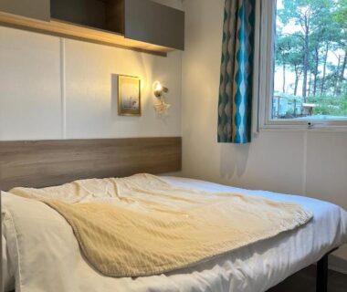 Intérieur de chambre avec lit double et fenêtre sur pins du camping On est trop bien ici