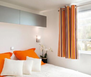 Chambre avec lit double coussins et rideaux orange au Paradis Des Dombes