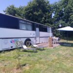 Sur la pelouse du camping à la ferme bus aménagé avec parasol et chaises Pépère