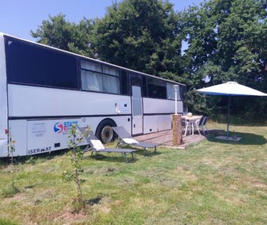 Sur la pelouse du camping à la ferme bus aménagé avec parasol et chaises Pépère