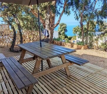 Terrasse ombragée avec table en bois et parasol avec vue mer au camping Piana