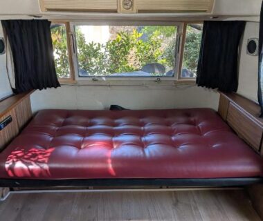 Intérieur de caravane avec banquette rouge et fenêtre sur la végétation au camping Pooh’s Belle
