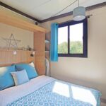 Chambre avec lit double et fenêtre donnant sur la nature au camping RAS L'BOL