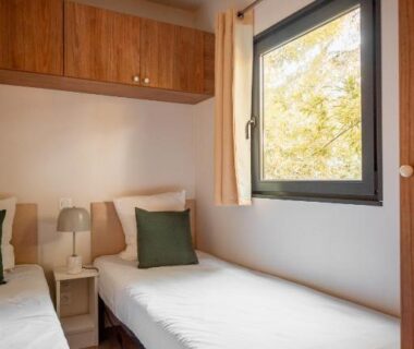 Chambre avec deux lits et fenêtre donnant sur arbres au camping Rives d'Arc