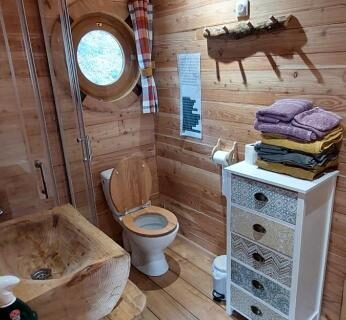 Salle de bain en bois avec lavabo et hublot dans la Roulotte Le Coq La Mazille