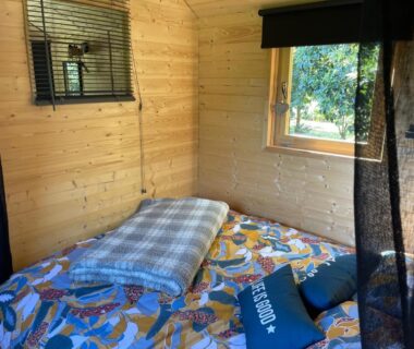 Intérieur en bois avec lit et fenêtre donnant sur la végétation dans la Roulotte