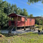 Sur la pelouse une roulotte rouge avec terrasse et table de pique-nique dans la Roulotte hébergement atypique