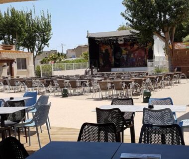 Terrasse extérieure avec tables et scène au camping SABLE DU MIDI chez gégé