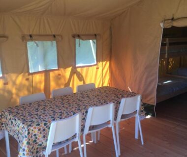Intérieur de tente avec table à nappe fleurie chaises et lits superposés du SafariLodge 6 persoons