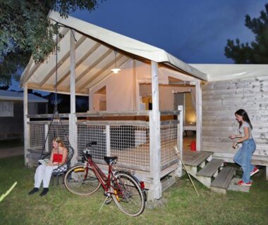 Terrasse éclairée de mobil-home avec vélos et personnes assises au Seasonova Camping Les 7 iles