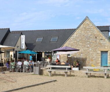 Façade en pierre avec terrasse et parasols du Seasonova Camping Les 7 iles