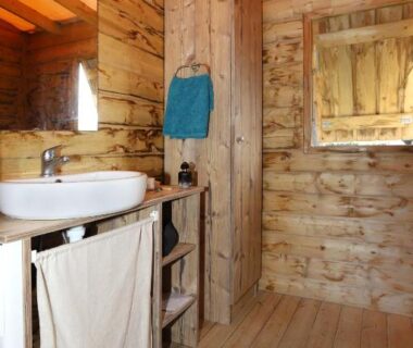Salle de bain en bois avec lavabo et hublot dans le Seasonova Camping Les 7 iles