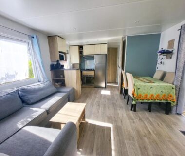 Salon avec canapé et kitchenette dans le mobil home Sevservices à La Réserve